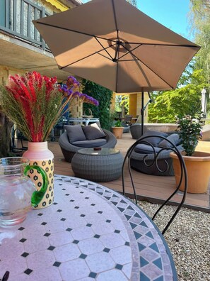 Un'area patio con mobili da esterno, un tavolo rotondo con piano in piastrelle decorate e un vaso ornamentale con fiori.