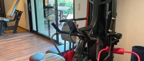 Ein Heimfitnessraum mit Ergometer, einer Bank und einem Krafttrainer.