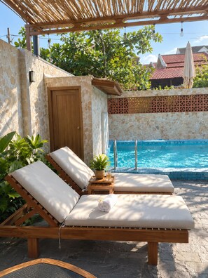 Ein Poolbereich mit Holzliegen, einer Steinmauer und einem Pool.