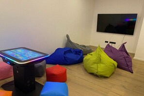 Ein Zimmer mit einer Spielkonsole, bunten Sitzsäcken und einem Fernseher an der Wand.