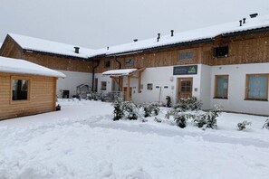 Ein schneebedecktes Gebäude mit Holzfassade, einer überdachten Außenbestuhlung und einem Schild, das auf ein Restaurant oder Café hinweist.