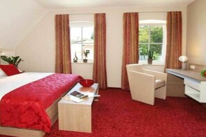 Ein Hotelzimmer mit Bett, Schreibtisch, Stuhl, kleinem Tisch und einem Fenster mit Vorhängen.