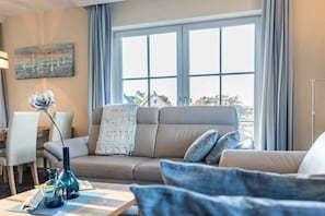 Ein modernes Wohnzimmer mit einer Couch, einem Couchtisch und Blick durch große Fenster.