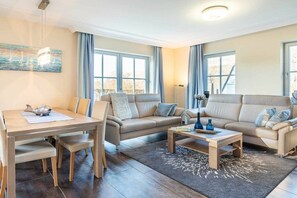 A modern living room with a sofa set, a coffee table, and a dining table with chairs. - Holiday home with 1 bedroom (Seebad Kölpinsee OT Stubbenfelde)