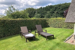 Ein Garten mit zwei Liegestühlen und einem Gebäude mit einem Reetdach.
