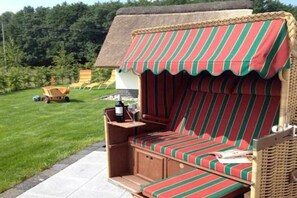 A thatched-roof outdoor seating area with a striped awning, a wooden bench, and a small table with a bottle and glass. - Holiday home with 1 bedroom (Seebad Kölpinsee OT Stubbenfelde)