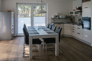 A modern kitchen with a dining table, chairs, and a refrigerator. - Holiday home oasis in the Müritz Lake Park (Röbel)