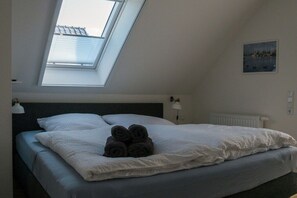 A bedroom with a skylight, a bed with white bedding, a headboard, a bedside lamp, and a painting on the wall. - Holiday home oasis in the Müritz Lake Park (Röbel)