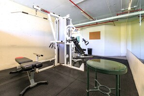 Ein Fitnessraum mit Trainingsgeräten, einer Bank und einem Glastisch.