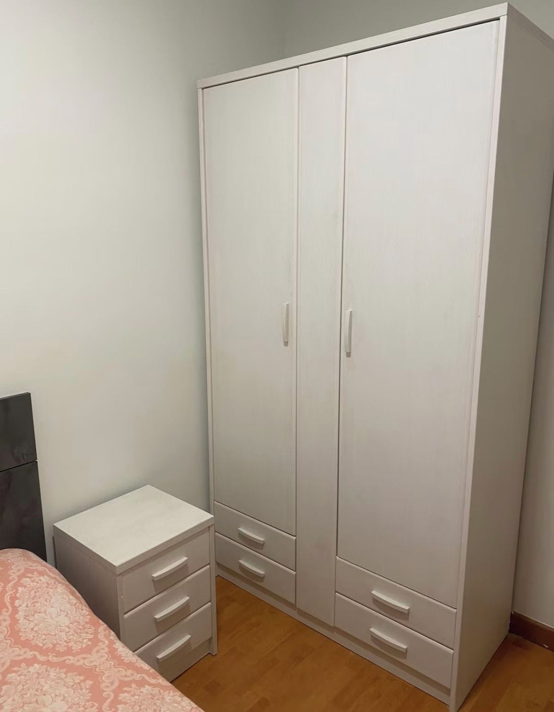 Un dormitorio con una cama, una mesita de noche y un armario con dos puertas y cajones.