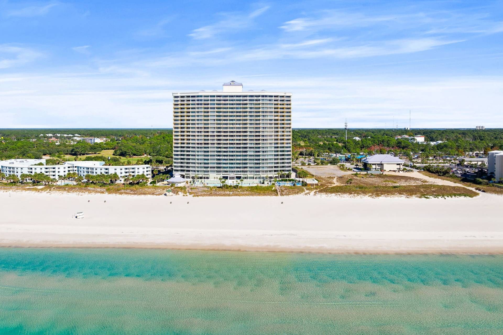 Ein Hochhaus-Hotel mit mehreren Stockwerken, ein Strand im Vordergrund und ein klarer Himmel.