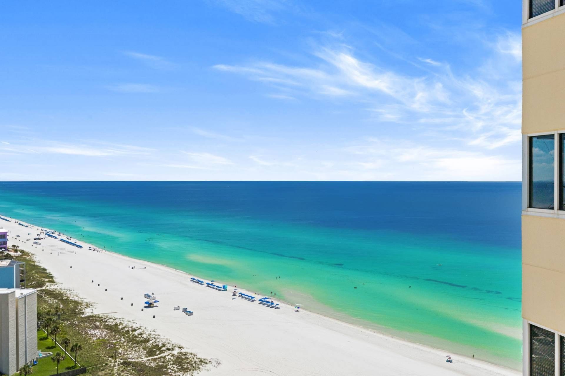 A beach with clear turquoise waters, a sandy shore, and a building with a balcony overlooking the beach.