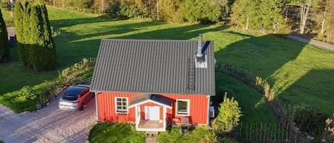Ein rotes Haus mit grauem Dach, einer Auffahrt und einem links geparkten Auto.
