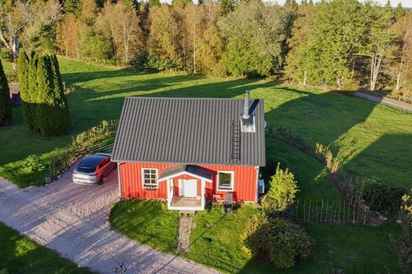 A red house with a grey roof, a driveway, and a car parked on the left.