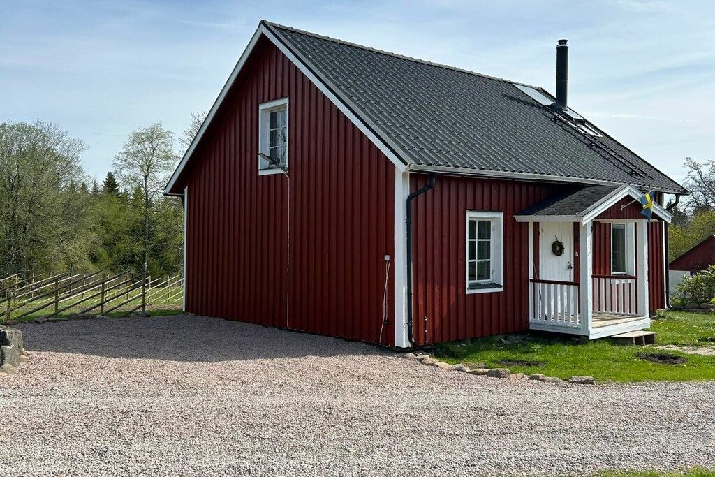 Een rood, laag gebouw met een veranda, schoorsteen en een grindpad.