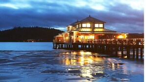 A waterfront building with a prominent tower, accessible via a pier, and a reflective water surface.