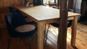 A wooden dining table with chairs, a hanging light fixture, a window with curtains, and a stove in a cabin-style room.
