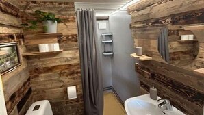 A bathroom with a rustic wooden wall design, a white toilet, a sink with a mirror, and a shower curtain.