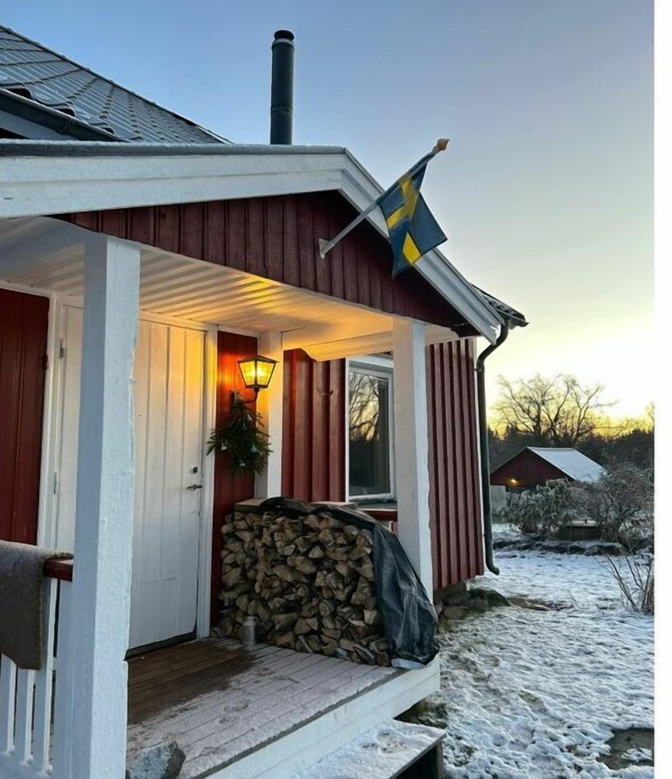Una casa de madera con porche, una bandera y un montón de leña.