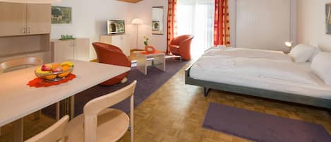 Quarto de hotel moderno com teto de madeira, área de refeições com mesa e cadeiras, cama e televisão.