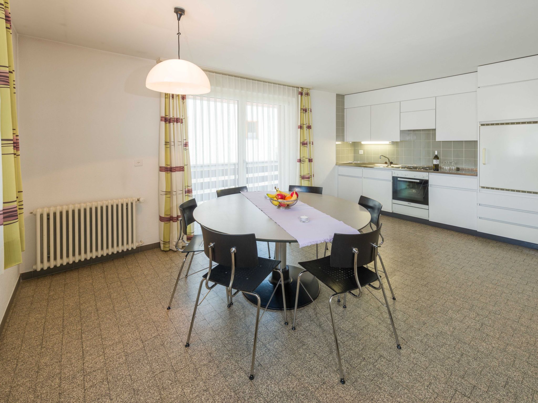 A modern kitchen with white cabinets, a dining table with chairs, and a fruit bowl on the table.