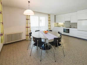Une cuisine moderne avec des meubles blancs, une table à manger avec des chaises et un panier de fruits posé sur la table.