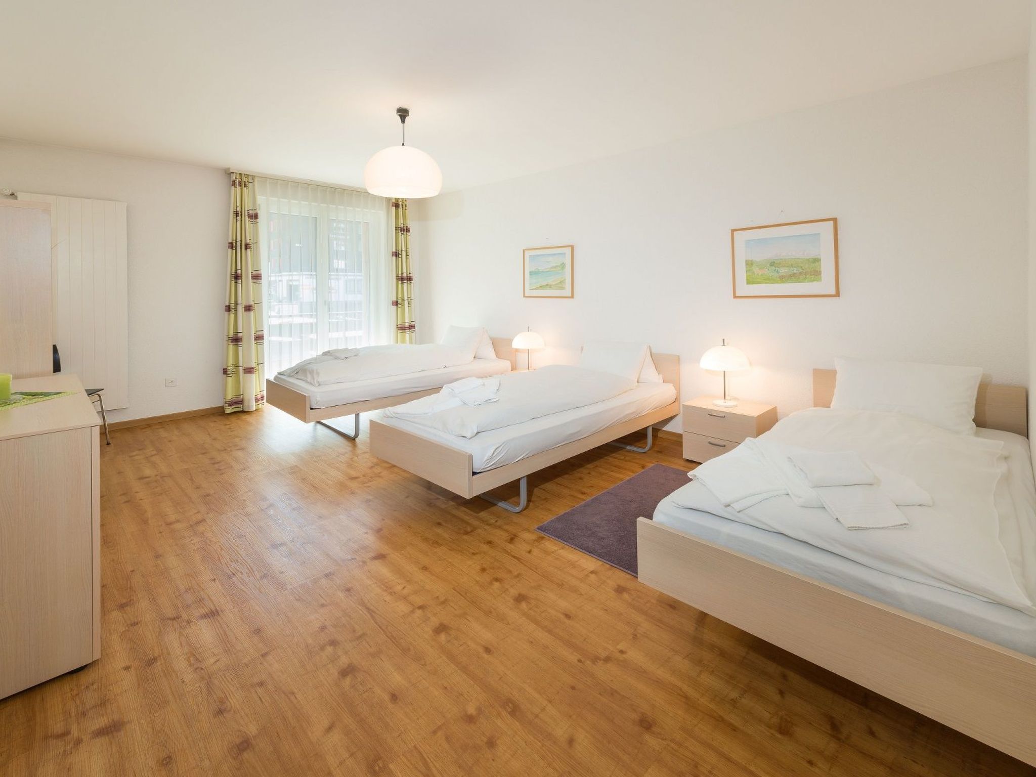 A hotel room with two single beds, a desk, and a window with curtains.