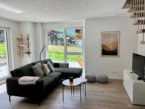 Ein modernes Wohnzimmer mit einer schwarzen Couch, einem Couchtisch und einer TV-Konsole.