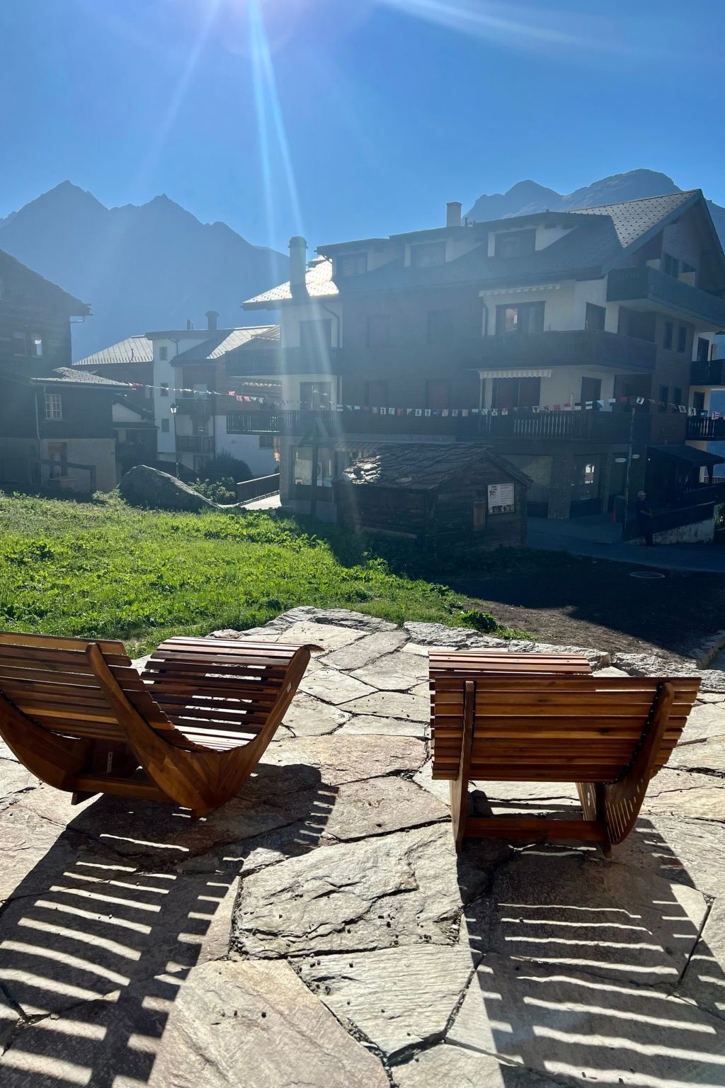 Two wooden benches on stone pavement with a mountainous backdrop and buildings.