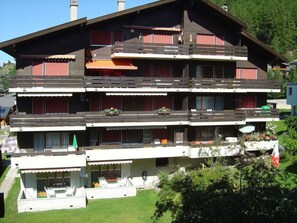 A multi-story building with balconies, a garden area, and a flag. - Soleil, (Grächen), 1699 by Interhome (Grächen)