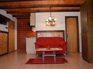 A room with a red sofa, a small table, a red rug, a wooden ceiling, and a door. - Soleil, (Grächen), 1699 by Interhome (Grächen)
