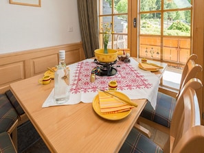 A dining table with a white tablecloth, wooden chairs, and a window with a view of greenery. - Försterli West, (Grächen), 3002 by Interhome (Grächen)