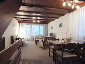 A cozy room with a wooden ceiling, a dining table with chairs, a sofa, and a window with curtains. - Ferienwohnungen Gsteinetgufer, (Grächen), by Interhome (Grächen)