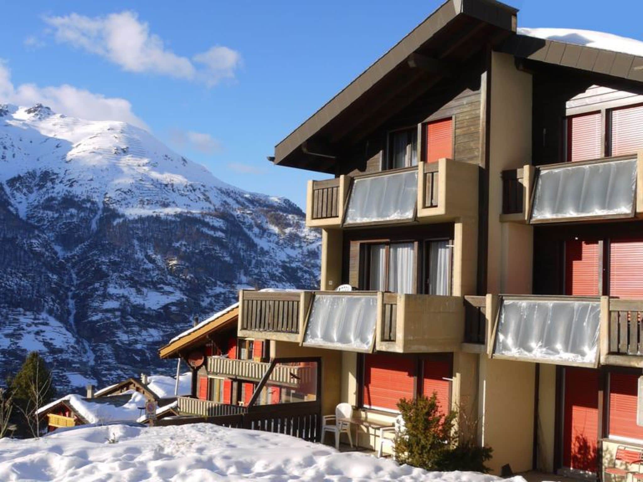 Un edificio de varios pisos con balcones, con una imponente montaña nevada de fondo.