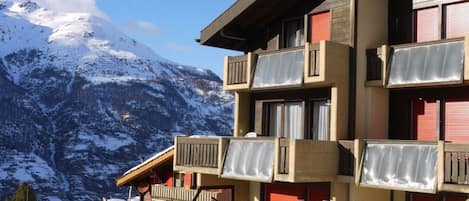Un edificio de varios pisos con balcones, con una imponente montaña nevada de fondo.