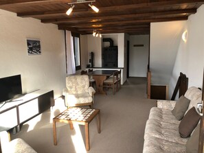 A cozy living room with a television, a patterned sofa, a wooden coffee table, and a dining area with a table and chairs. - Ferienwohnungen Gsteinetgufer, (Grächen), by Interhome (Grächen)