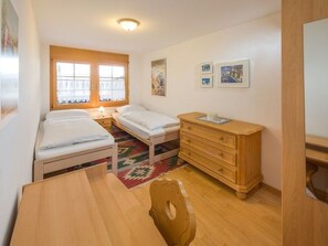 A small, well-lit room with two single beds, a wooden dresser, a desk, and a chair. - Beatrice, (Grächen), 1060 by Interhome (Grächen)