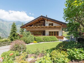 A two-story chalet with a balcony, surrounded by a well-maintained garden and mountains in the background. - Försterli Ost, (Grächen), 3003 by Interhome (Grächen)