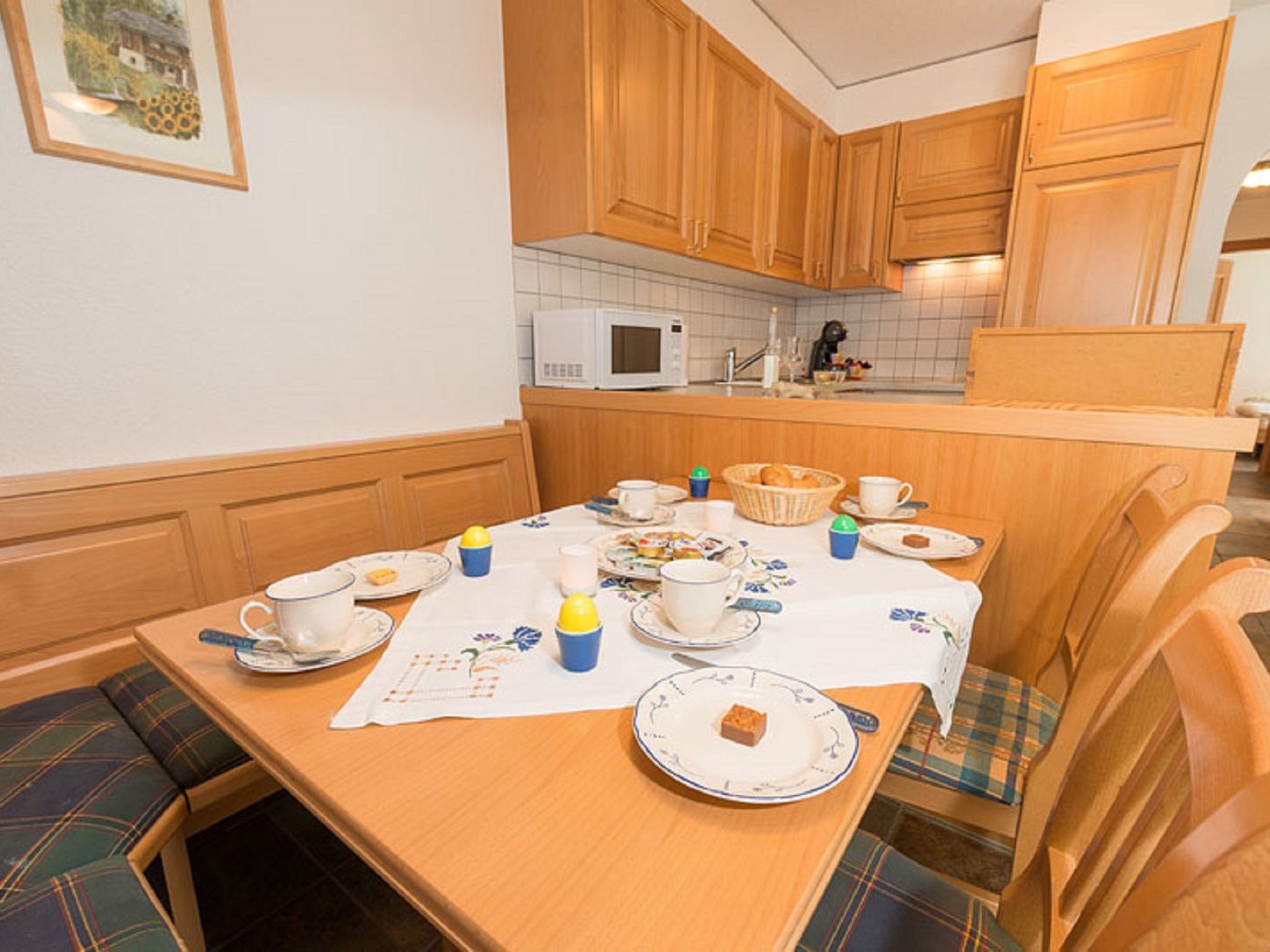 A cozy kitchen with wooden cabinets, a microwave, and a dining table set for a meal.