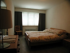 A bedroom with a bed, a chair, a lamp, and a window with curtains. - Brunegghorn 4, (Grächen), 1930 by Interhome (Grächen)