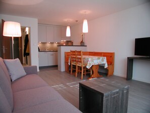 A modern living room with a sofa, a dining table with chairs, a kitchen area, and a TV on a stand. - Brunegghorn 4, (Grächen), 1930 by Interhome (Grächen)