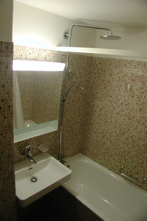 A bathroom with a white sink, a mirror, a shower with a handheld showerhead, and a tiled wall. - Brunegghorn 4, (Grächen), 1930 by Interhome (Grächen)
