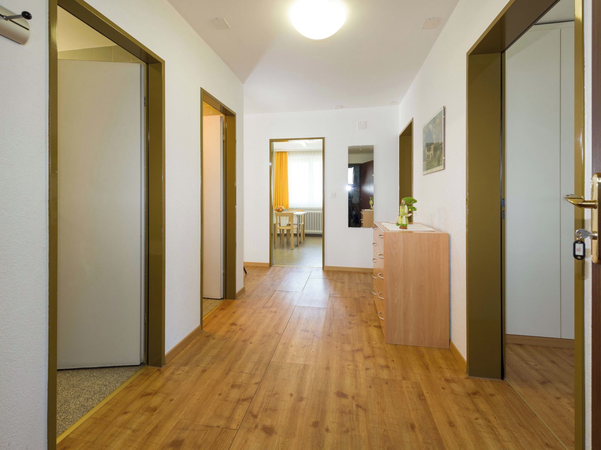 A hallway with wooden flooring, white walls, and doors leading to other rooms.