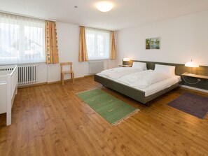 A hotel room with a bed, two bedside tables, a chair, a radiator, and a window with curtains. - Ferienwohnungen Postgebäude, (Grächen), by Interhome (Grächen)