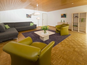Ein modernes Wohnzimmer mit einem grauen Sofa, grünen Sesseln, einem Couchtisch mit Blumen und Holzboden.