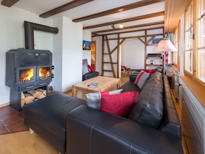 Ein gemütliches Wohnzimmer mit einem schwarzen Ledersofa, einem Holztisch und einem Kamin mit sichtbaren Holzscheiten.