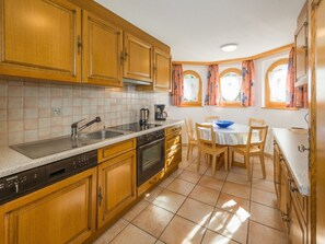 A kitchen with wooden cabinets, a dishwasher, an oven, a coffee maker, and a dining table with chairs. - Paradiso 2, (Grächen), 2003 by Interhome (Grächen)