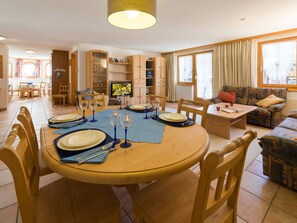 Uma sala de jantar com uma mesa redonda posta para quatro pessoas, rodeada por cadeiras de madeira.