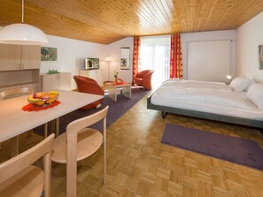 A modern hotel room with a wooden ceiling, a dining area with a table and chairs, a bed, and a TV on a cabinet. - Ferienwohnungen Postgebäude, (Grächen), by Interhome (Grächen)