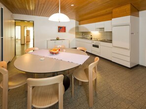 A modern kitchen with white cabinets, a round dining table with chairs, and a pendant light. - Ferienwohnungen Postgebäude, (Grächen), by Interhome (Grächen)